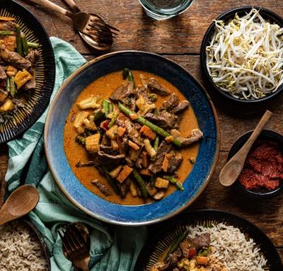 a wooden table topped with bowls of food and utensils . a wooden table topped with bowls of food and utensils .