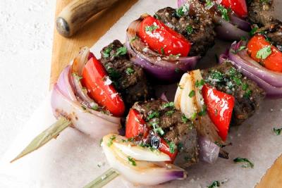Grilled beef skewers with red capcicum and red onions, garnished with herbs.