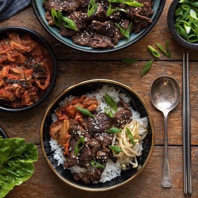 A Korean meal featuring a bulgogi and kimchi rice bowl, separate bowls of bulgogi and kimchi, and fresh lettuce on a wooden table.