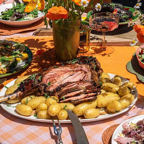 a white plate topped with a plate of roast lamb surrounded by potatoes on a checked table cloth a white plate topped with a plate of roast lamb surrounded by potatoes on a checked table cloth