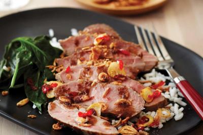Sliced lamb rumps, white rice, spinach, and crispy fried shallots with red chilies on a black plate.
