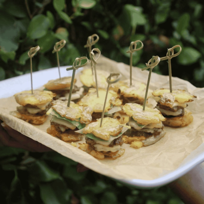 Mini sliders with crispy potato tops and decorative skewers on a tray.