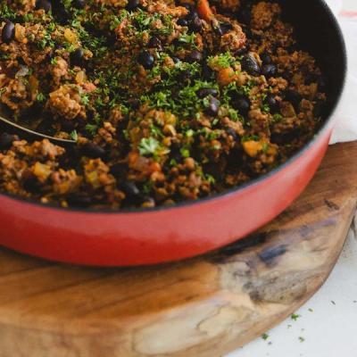 Red skillet of mince and black beans with parsley on a wooden board. Red skillet of mince and black beans with parsley on a wooden board.