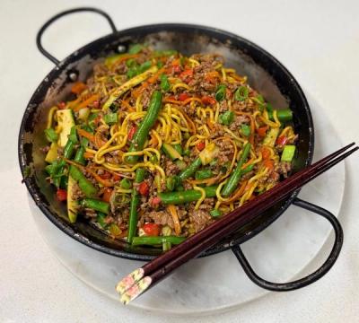 a pan filled with noodles , meat and vegetables with chopsticks on a plate . a pan filled with noodles , meat and vegetables with chopsticks on a plate .