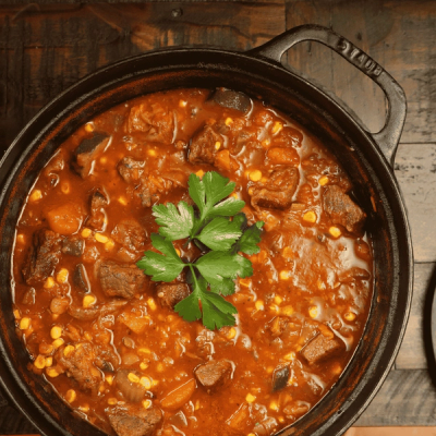 Overhead shot of a rich beef and corn stew in a black cast-iron pot, garnished with parsley.