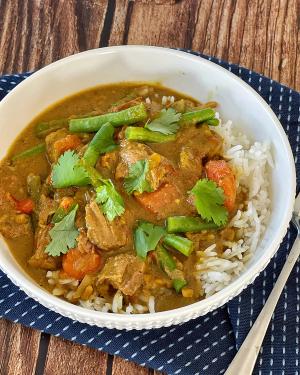 a bowl of beef curry with rice and vegetables on a wooden table . a bowl of beef curry with rice and vegetables on a wooden table .
