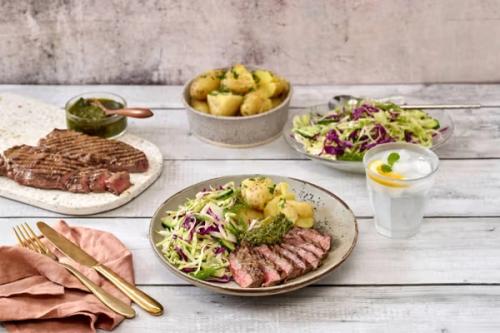 Sliced grilled steak, roasted potatoes, and a colorful cabbage salad with green sauce and lemon water. Sliced grilled steak, roasted potatoes, and a colorful cabbage salad with green sauce and lemon water.