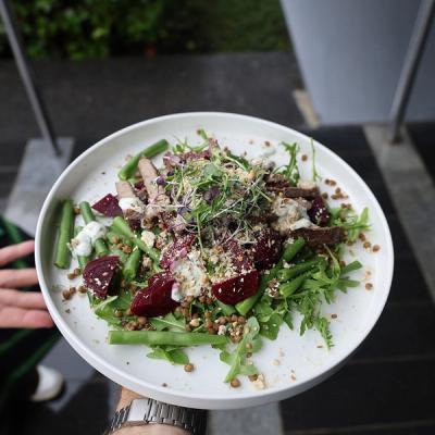 a person is holding a white plate with a beetroot, lentil and rump steak salad on it. 