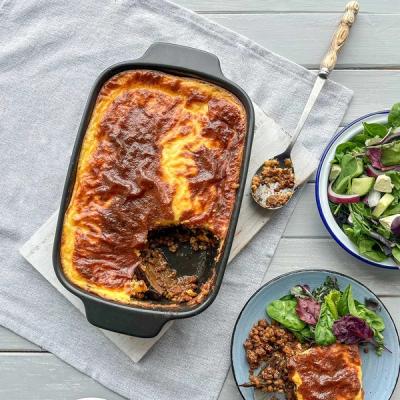 a casserole dish with a spoon in it is sitting on a table next to a plate of food . a casserole dish with a spoon in it is sitting on a table next to a plate of food .