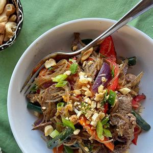 a white bowl filled with noodles , meat and vegetables with a fork in it .