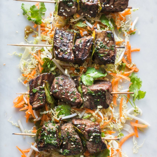 Grilled beef skewers with sesame seeds and green herbs on a bed of Asian slaw. Grilled beef skewers with sesame seeds and green herbs on a bed of Asian slaw.