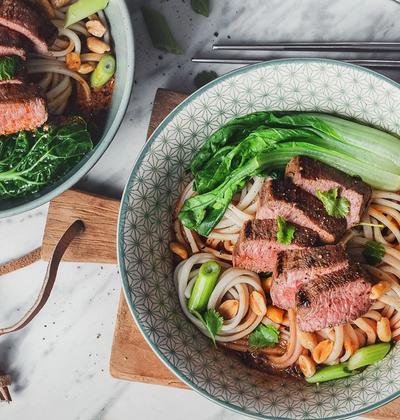 a bowl of noodles with meat and vegetables next to a bowl of peanuts a bowl of noodles with meat and vegetables next to a bowl of peanuts