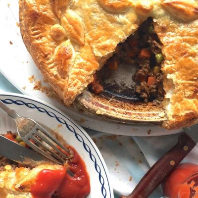 a meat pie with a slice taken out of it is on a plate next to a bowl of ketchup. a meat pie with a slice taken out of it is on a plate next to a bowl of ketchup.