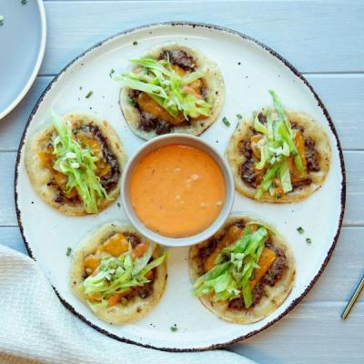 Five mini tacos with ground meat, cheese, and lettuce, arranged around a bowl of orange sauce on a white plate. Five mini tacos with ground meat, cheese, and lettuce, arranged around a bowl of orange sauce on a white plate.