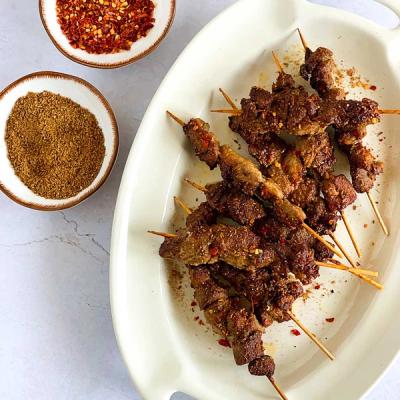 a white plate topped with meat skewers next to a bowl of spices .