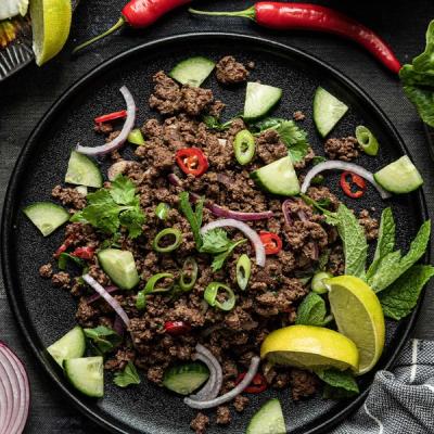 a black plate topped with ground beef, cucumbers, onions, peppers and mint leaves. a black plate topped with ground beef, cucumbers, onions, peppers and mint leaves.