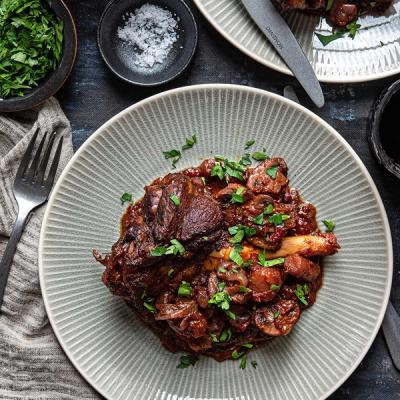 a plate of food with lamb shanks braised in red wine on a table with a fork .