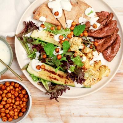 A plate of sliced lamb rump, grilled zucchini, roasted cauliflower, mixed greens, crispy chickpeas, pita, and creamy white dressing. A plate of sliced lamb rump, grilled zucchini, roasted cauliflower, mixed greens, crispy chickpeas, pita, and creamy white dressing.