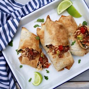 three burritos are sitting on a white plate with lime wedges .