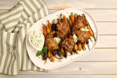 Lamb chops with roasted rainbow carrots and mint yogurt sauce on a white platter. Lamb chops with roasted rainbow carrots and mint yogurt sauce on a white platter.