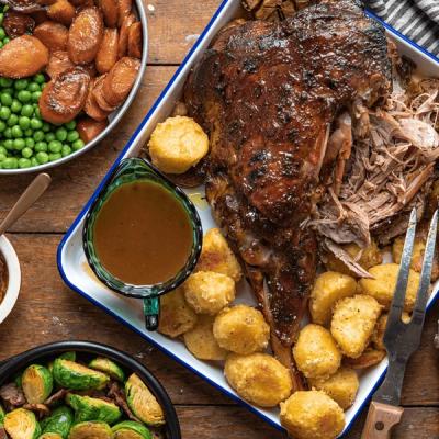a tray of lamb , potatoes , carrots , peas and gravy on a wooden table .