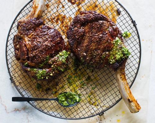 two steaks are sitting on a cooling rack with a spoon .