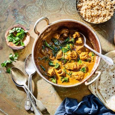 Overhead shot of chicken, mushroom, and spinach curry in a metal bowl, served with brown rice, flatbreads, and cilantro on an ornate golden tray.