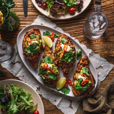 a white plate topped with stuffed sweet potatoes and guacamole on a wooden table . a white plate topped with stuffed sweet potatoes and guacamole on a wooden table .