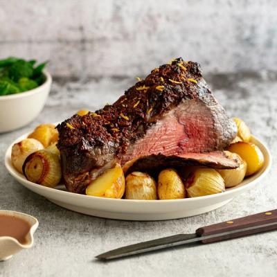 A sliced medium-rare roast beef with a zest-covered crust, surrounded by roasted potatoes and onions on a white platter. A sliced medium-rare roast beef with a zest-covered crust, surrounded by roasted potatoes and onions on a white platter.
