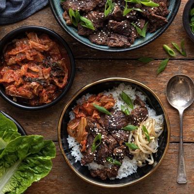 An overhead view of a Korean meal featuring bulgogi, kimchi, a rice bowl, and fresh lettuce on a wooden table. An overhead view of a Korean meal featuring bulgogi, kimchi, a rice bowl, and fresh lettuce on a wooden table.