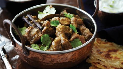 Copper bowl of meat curry with cilantro and spices, served with flatbread.