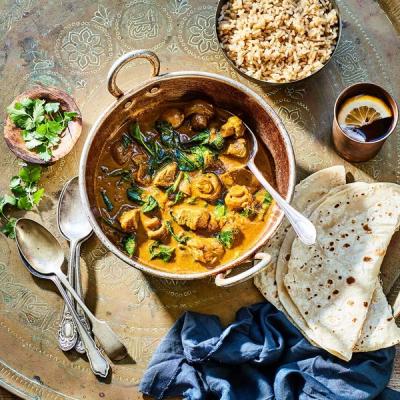 a bowl of chicken curry with rice and roti on a tray . a bowl of chicken curry with rice and roti on a tray .
