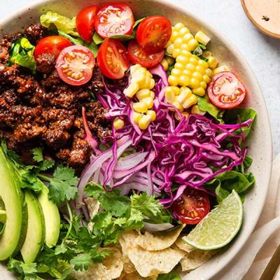 a close up of a bowl of food with, beef mince, tacos and tomatoes , corn , cabbage , onions and avocado . a close up of a bowl of food with, beef mince, tacos and tomatoes , corn , cabbage , onions and avocado .