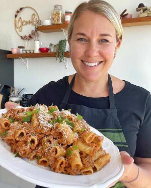 a woman is holding a plate of pasta and smiling . a woman is holding a plate of pasta and smiling .