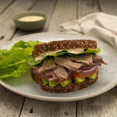 A roast beef sandwich on seeded whole-grain bread with lettuce, tomato, red onion, avocado, and sauce, served on a plate with extra lettuce. A roast beef sandwich on seeded whole-grain bread with lettuce, tomato, red onion, avocado, and sauce, served on a plate with extra lettuce.