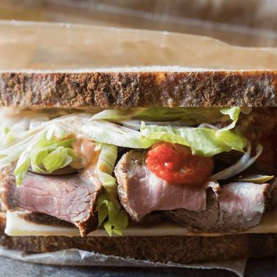 Roast lamb sandwich on dark bread with cheese, lettuce, sauce, and tomatoes. Roast lamb sandwich on dark bread with cheese, lettuce, sauce, and tomatoes.