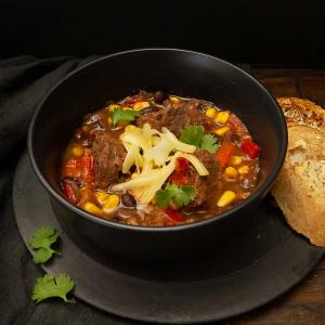 a bowl of beef soup with cheese and bread on a table