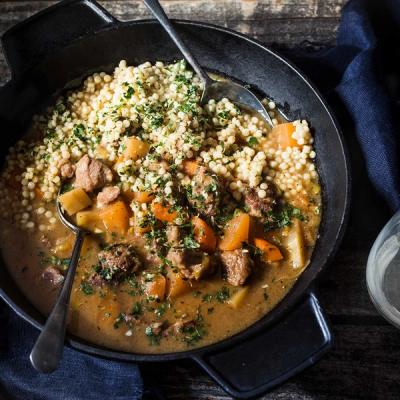 a casserole dish filled with stew and couscous with a spoon in it .