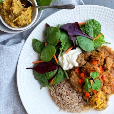 a white plate topped with rice , meat , spinach , carrots and sour cream .