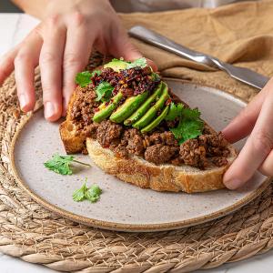 a person is holding a sandwich with avocado and meat on a plate .