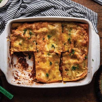 A pan of baked lasagna with a golden-brown cheesy top, garnished with herbs, and a few slices missing. A pan of baked lasagna with a golden-brown cheesy top, garnished with herbs, and a few slices missing.
