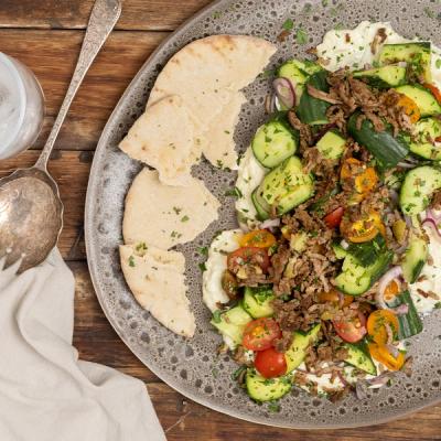 A plate with seasoned lamb mince, cucumbers, tomatoes, red onions, creamy sauce, and pita bread. A plate with seasoned lamb mince, cucumbers, tomatoes, red onions, creamy sauce, and pita bread.