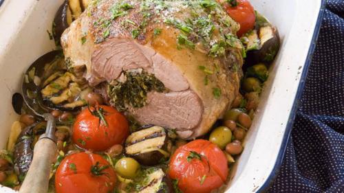 A stuffed roasted leg of lamb with tomatoes, eggplant, olives, and beans in a white enamel roasting pan. A stuffed roasted leg of lamb with tomatoes, eggplant, olives, and beans in a white enamel roasting pan.
