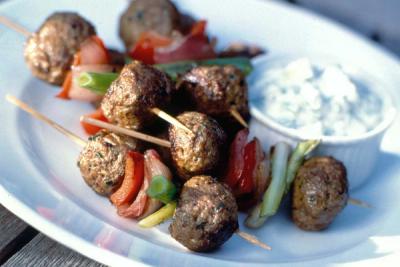 Meatball and vegetable skewers with a side of dip on a white plate. Meatball and vegetable skewers with a side of dip on a white plate.