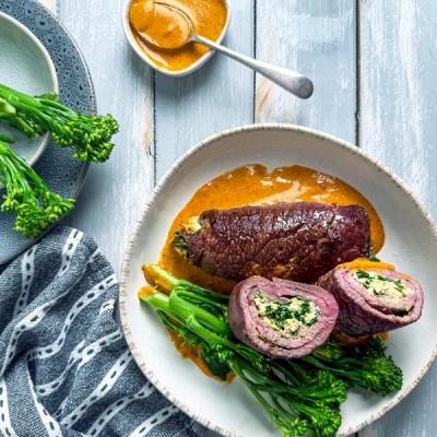 a plate of food with meat roulades, broccoli and sauce on a table .
