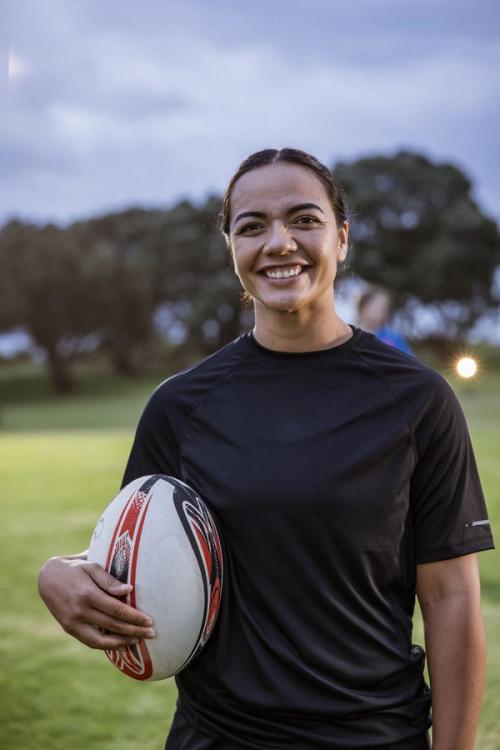a woman in a black shirt is holding a rugby ball