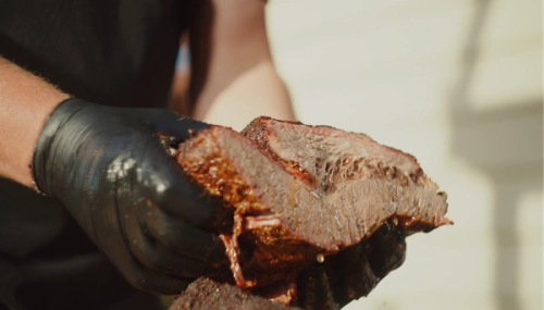 a person wearing black gloves holding a piece of meat