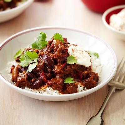 a bowl of chili with rice and sour cream on a table with a fork .
