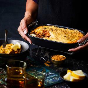 a person is placing a casserole dish on a table with a Shepherds pie in it