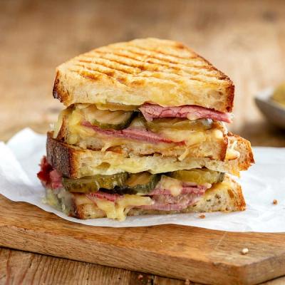 a corned beef toasted sandwich is stacked on top of each other on a wooden cutting board. a corned beef toasted sandwich is stacked on top of each other on a wooden cutting board.